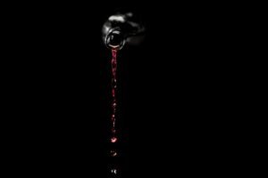 Red wine pouring from a sloped-shoulder Burgundy-style glass bottle